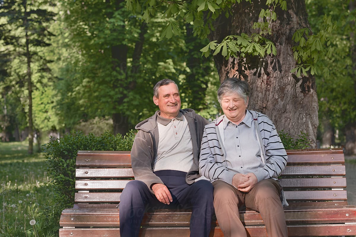 Elderly couple laughing on a bench in the park