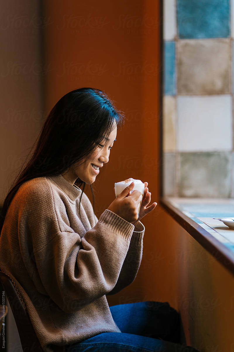 Cheerful Asian woman with cup of coffee in cafe