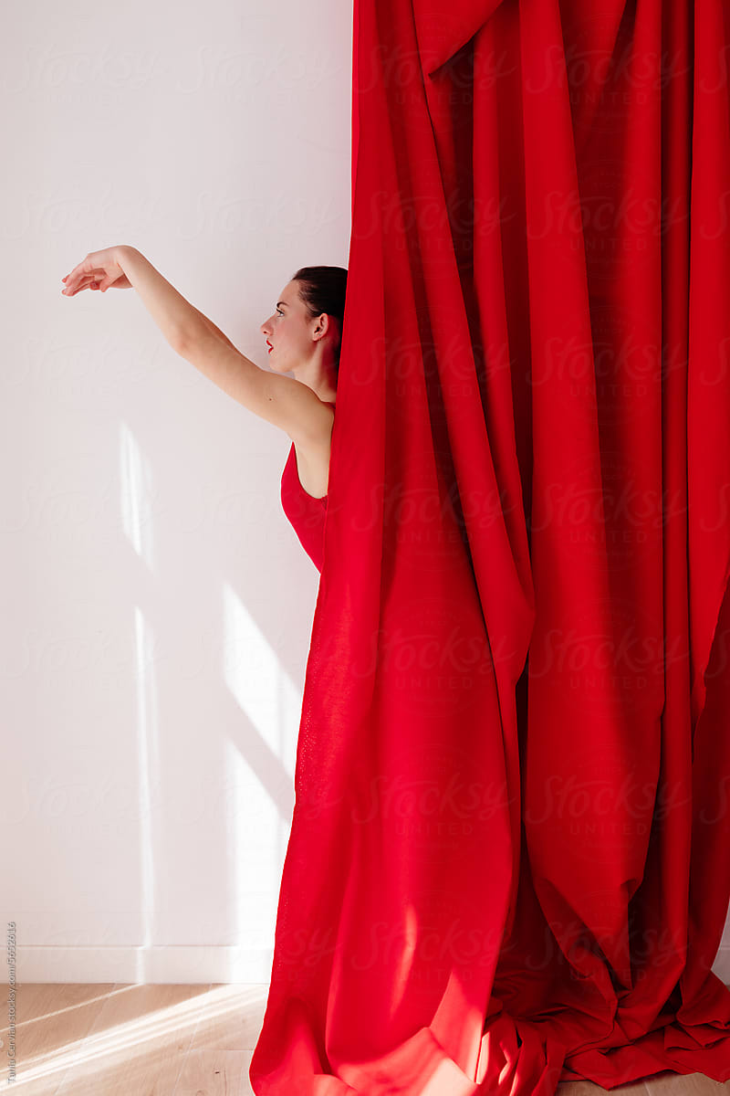 Young woman hiding waist downwards behind red curtain