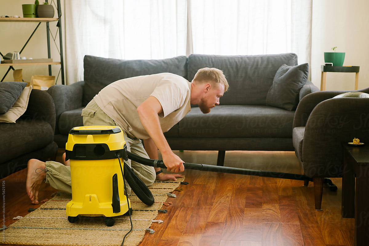 Blond-haired man vacuuming under the couch