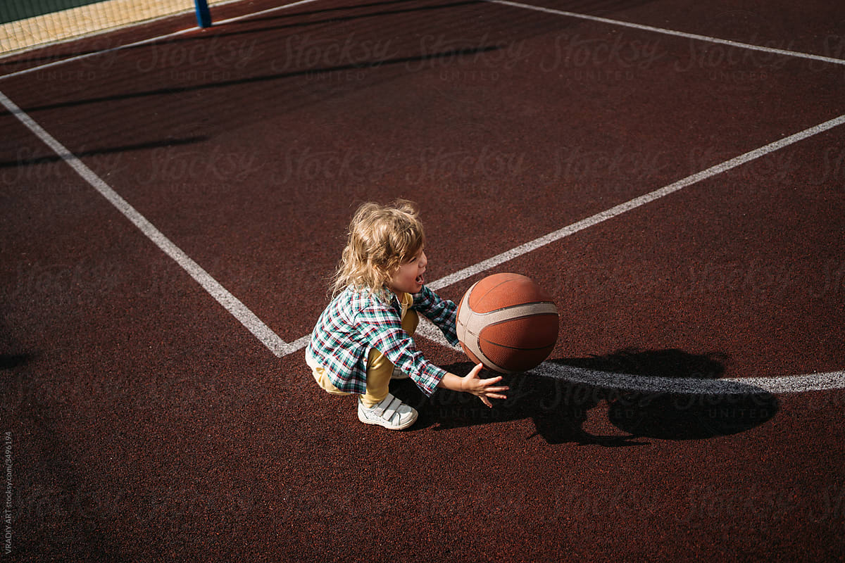 Little kid playing basketball ball on sports ground