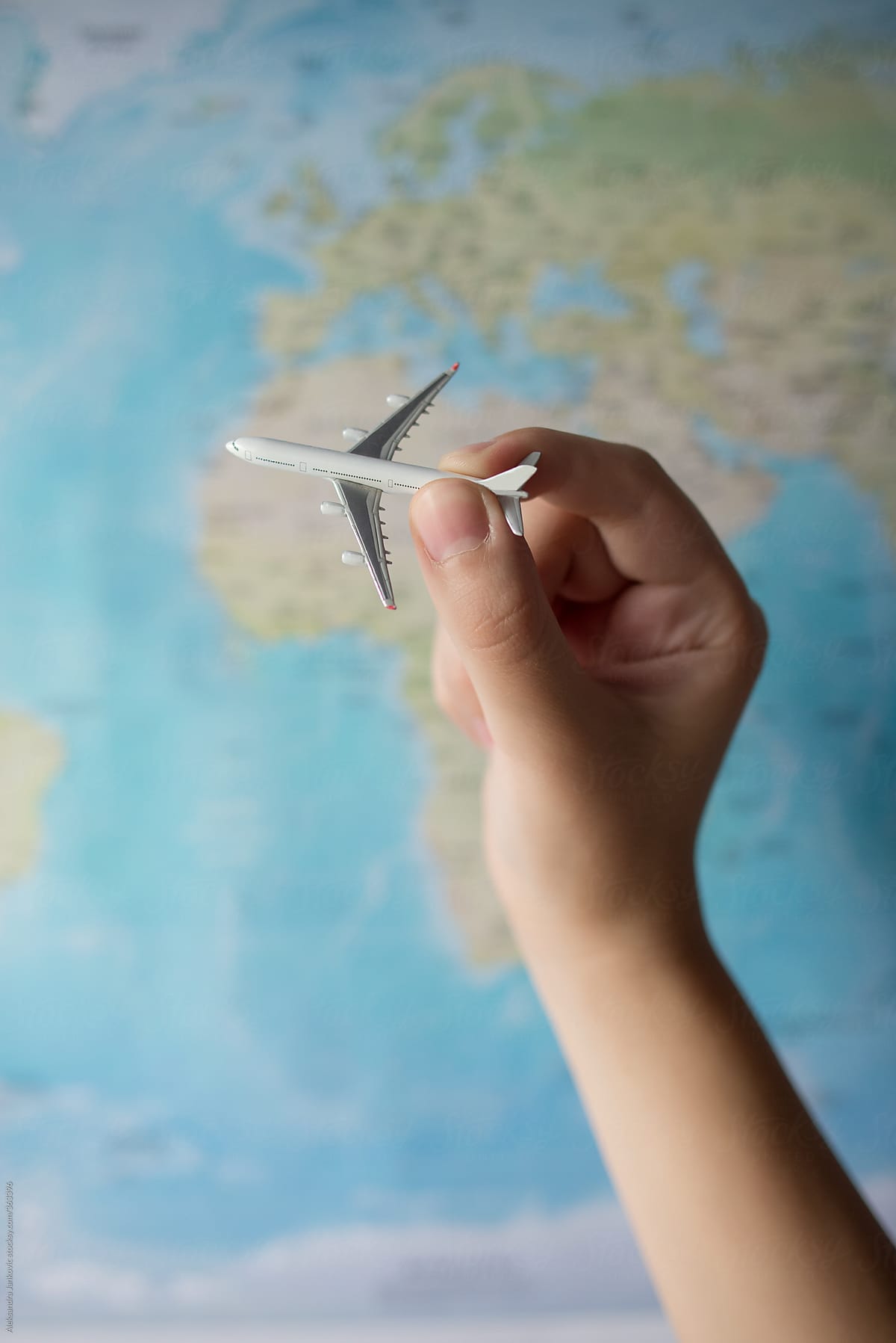 Person holding small airplane in front of the world\'s map