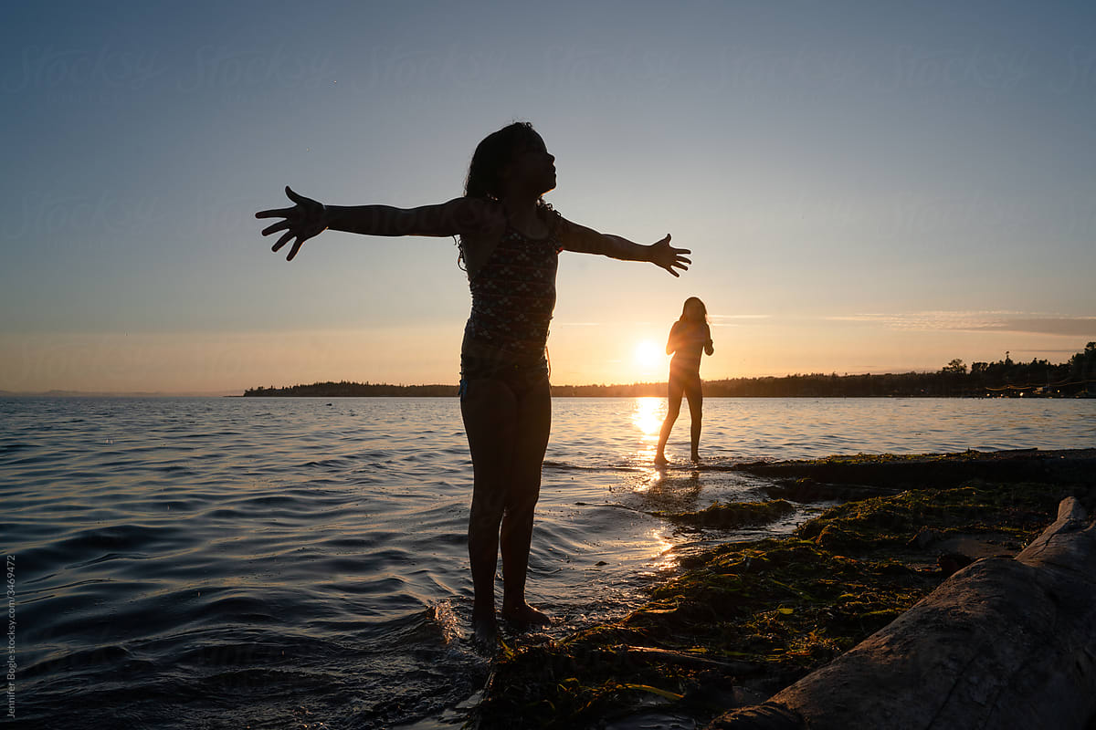 Silhouetted girl at beach throws arms wide