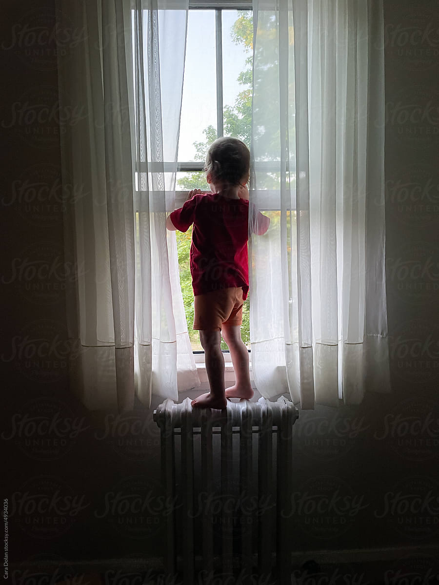 Toddler Stands on Radiator to Look Out Window