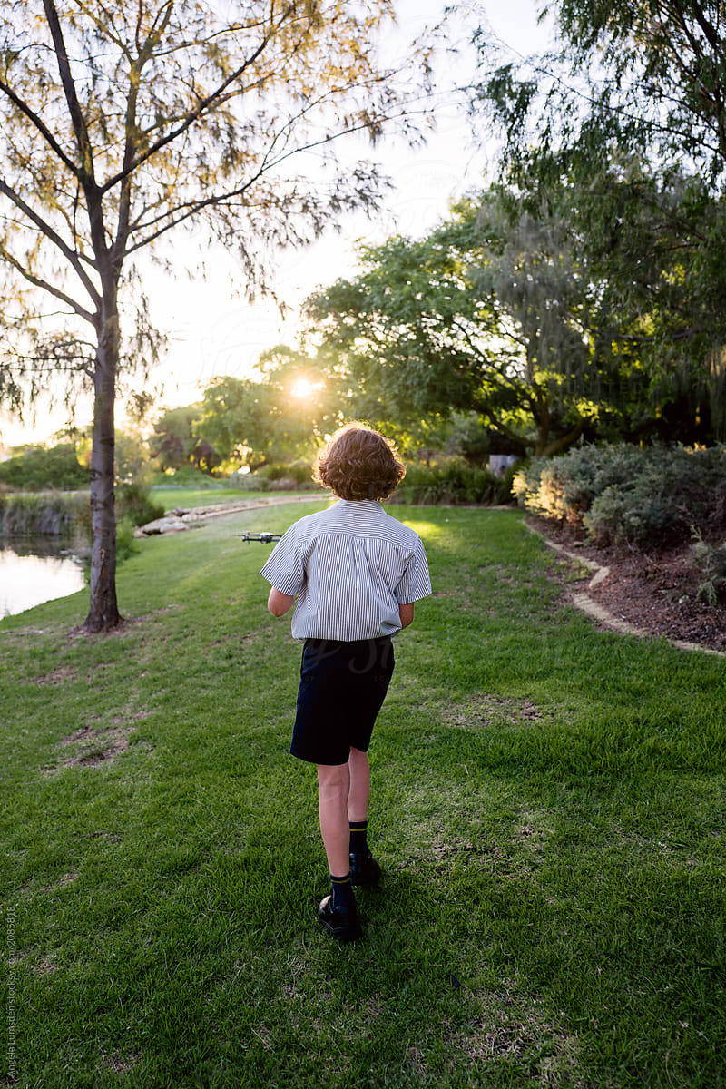 Boy walking with a low flying drone, viewed from behind