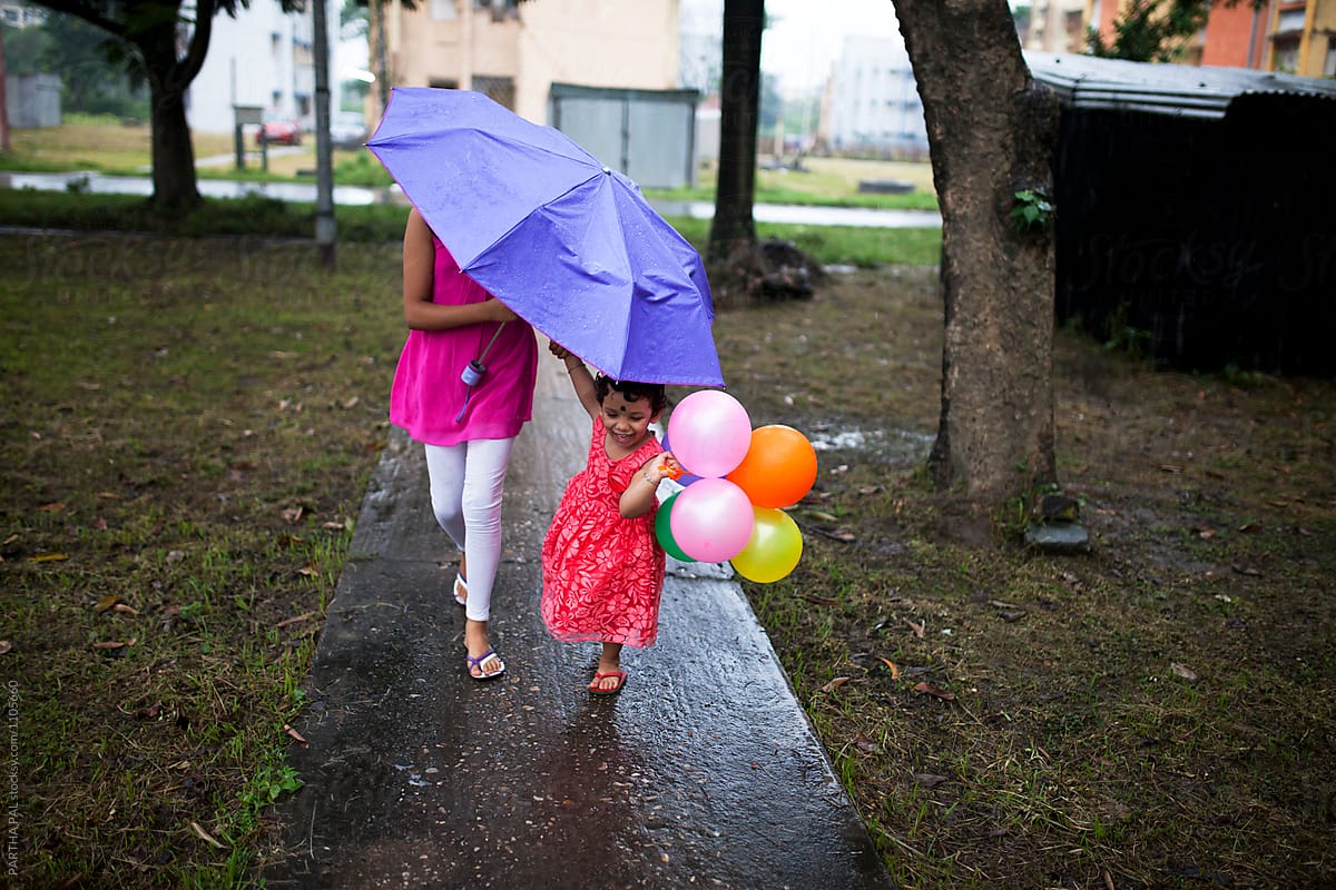 Sisters walking under one umbrella and holding balloons