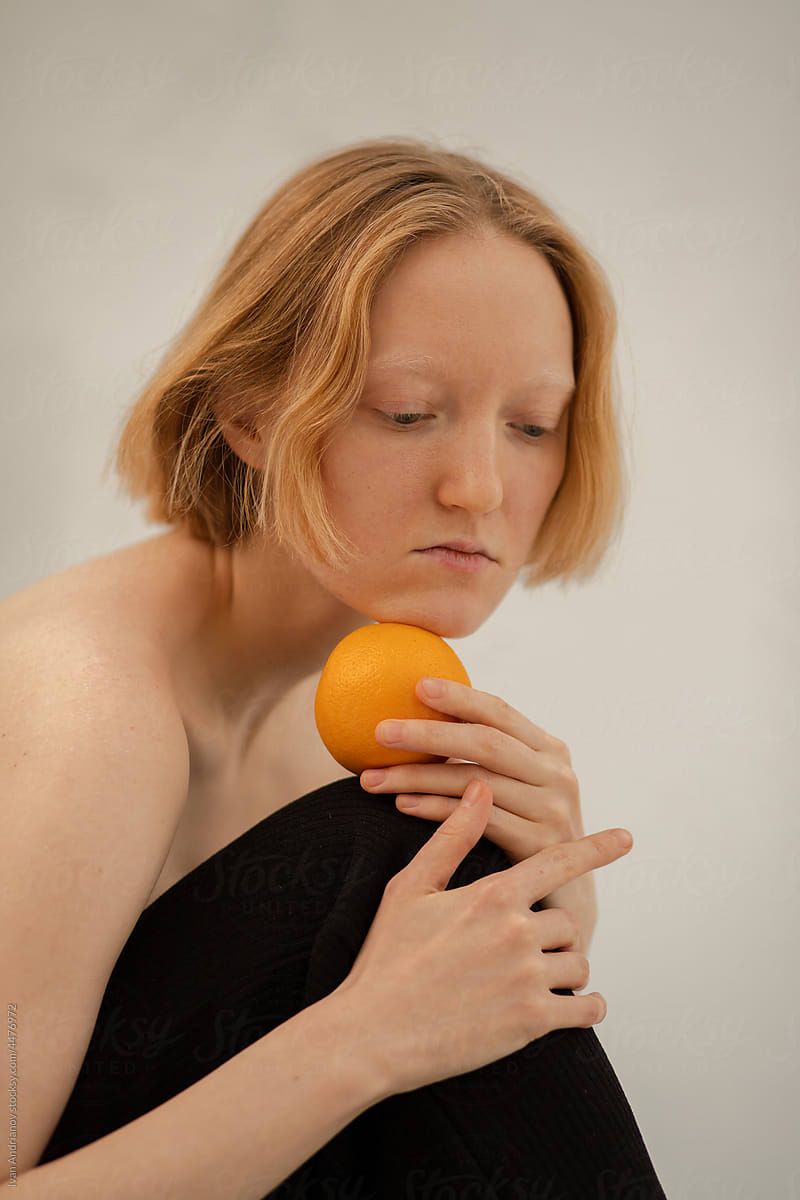 Young thoughtful blonde model posing with orange on grey background