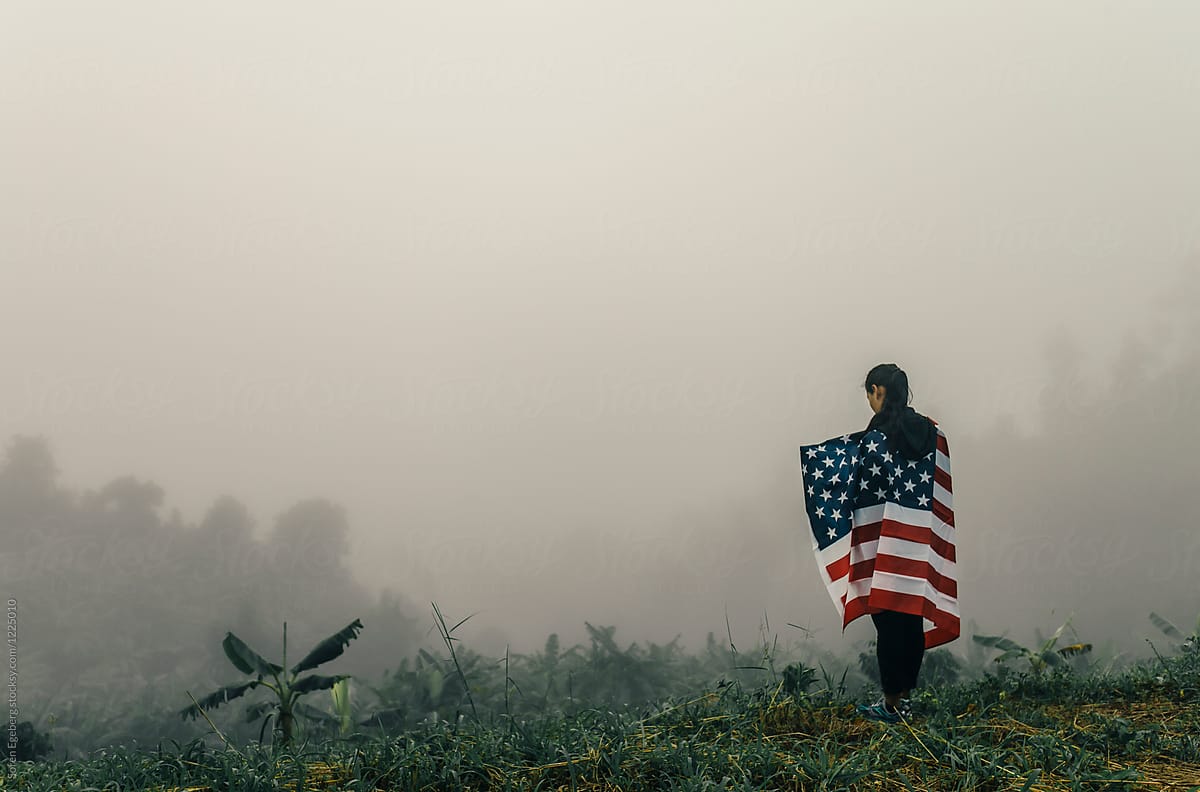 Ethnic woman carrying american flag in foggy landscape