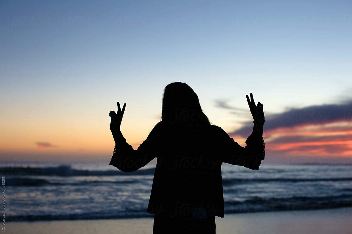 Teenage girl flashing peace signs at sunset