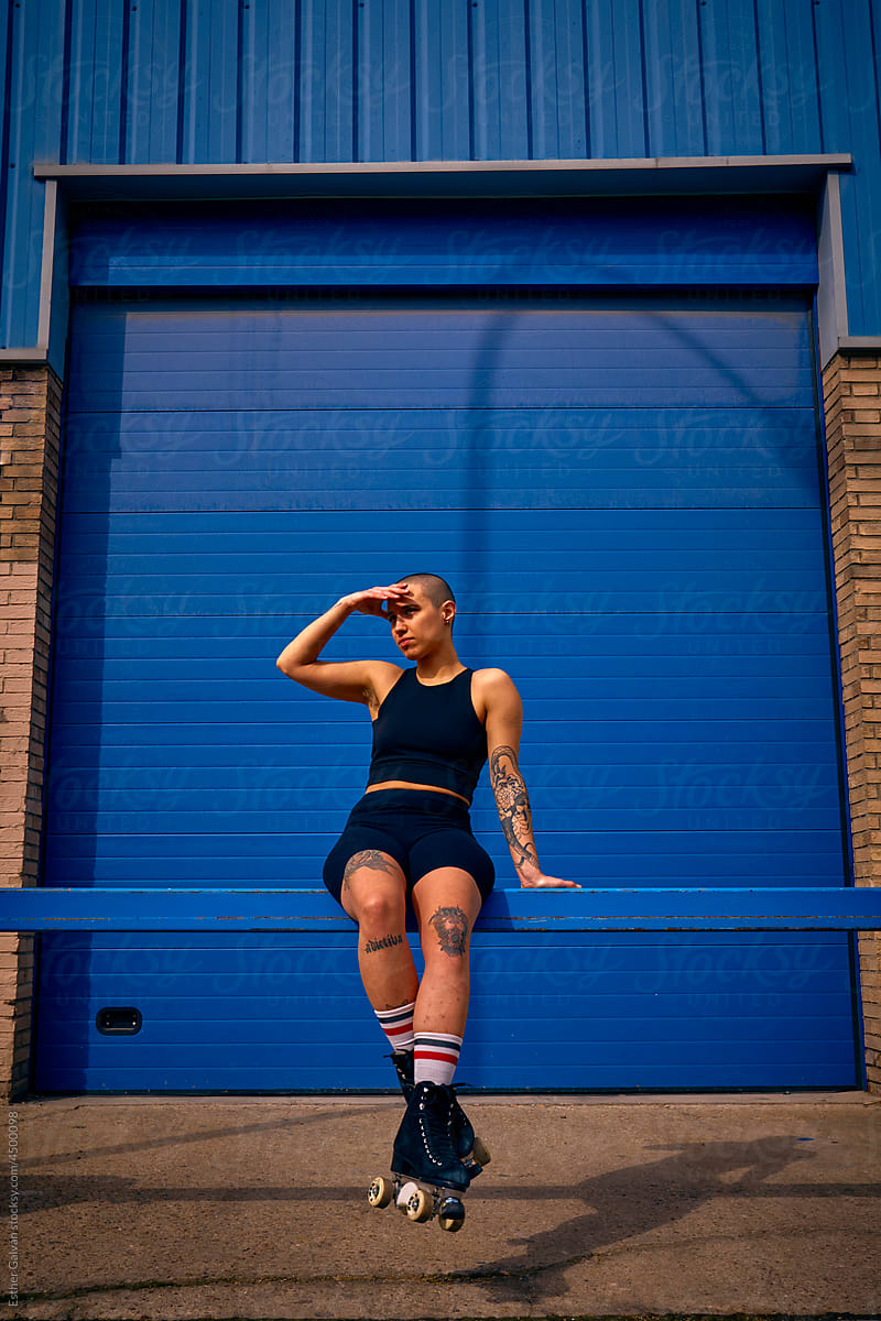 Non binary model at a blue door covering their face and wearing skates