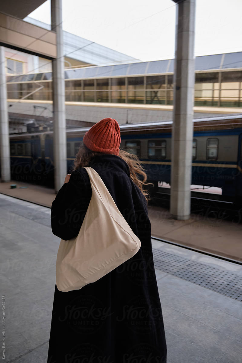 a girl in stylish clothes and a red hat with a bag on her shoulder walks through the train station
