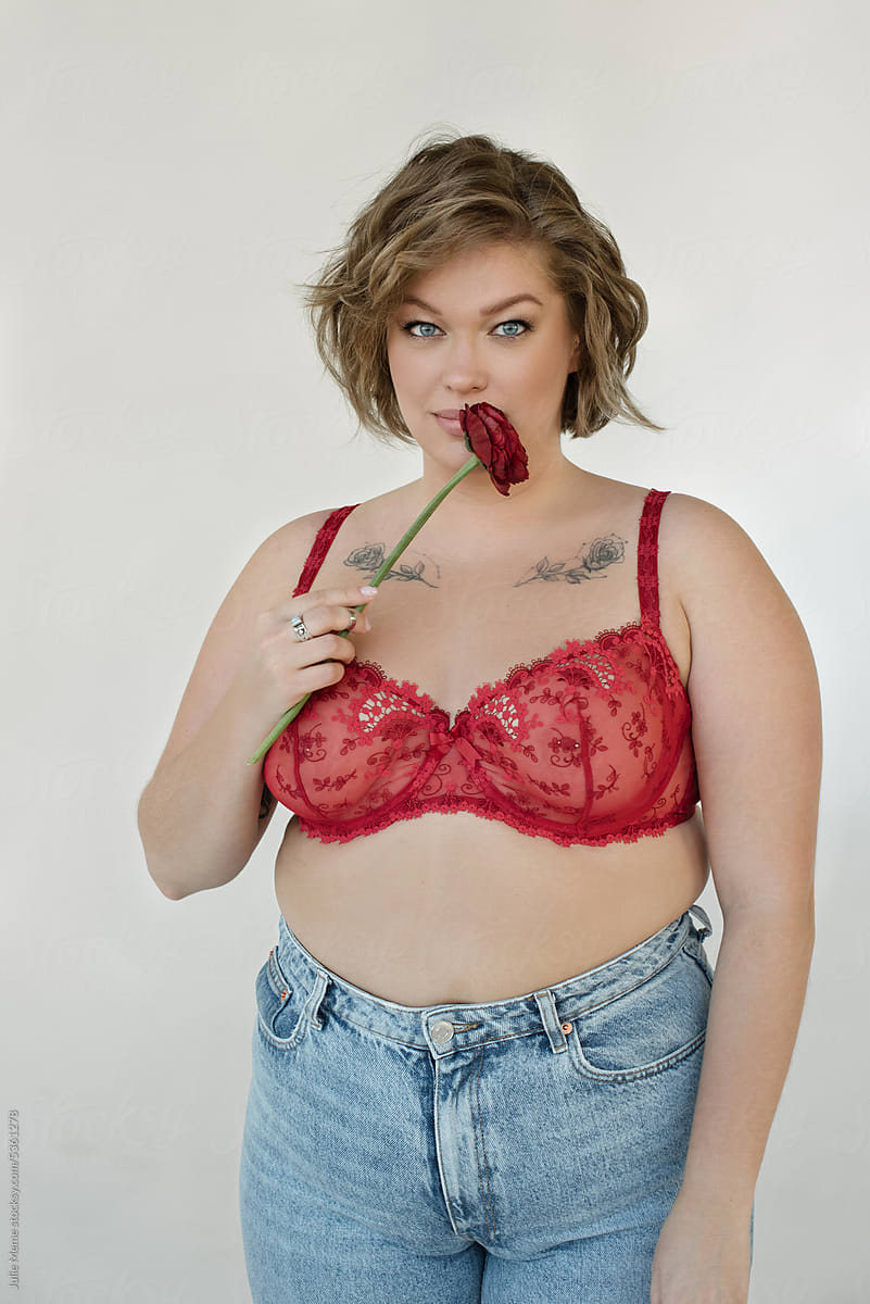 Attractive plus size woman in red bra and jeans holding rose