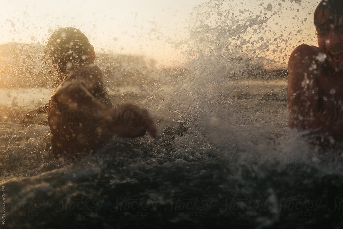 Two young boys playfully splash around the ocean at dusk