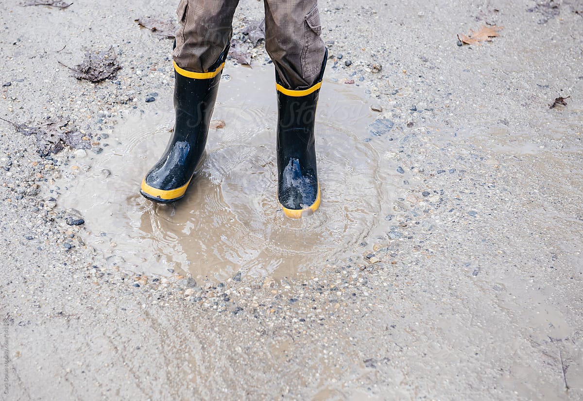 Child wearing rubber boots splashes in a mud puddle