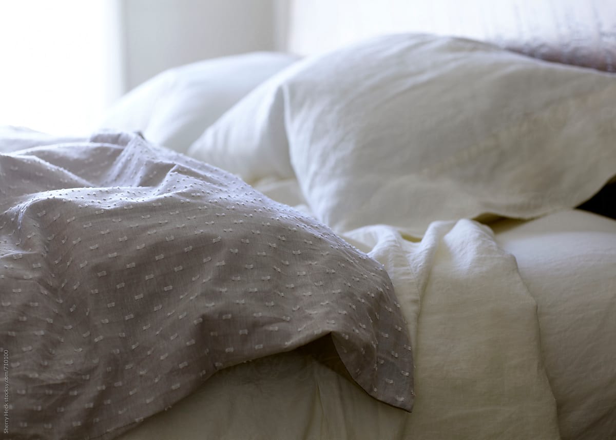 Side shot of a slightly disheveled bed with white fluffy pillows and linen sheets