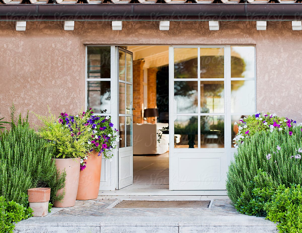 Shurbs and flowering plants in pots in front of big front door in rural building in Tuscany countryside, Italy