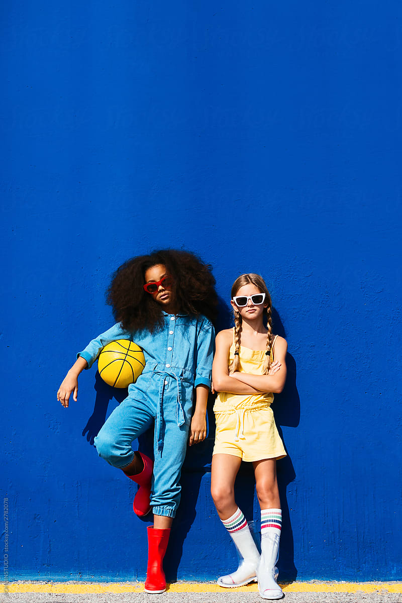 Trendy multiethnic friends in sunglasses holding ball while standing on street