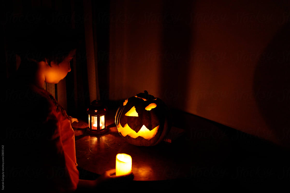 Little girl in front of a Halloween pumpkin in a dark room lit by candles
