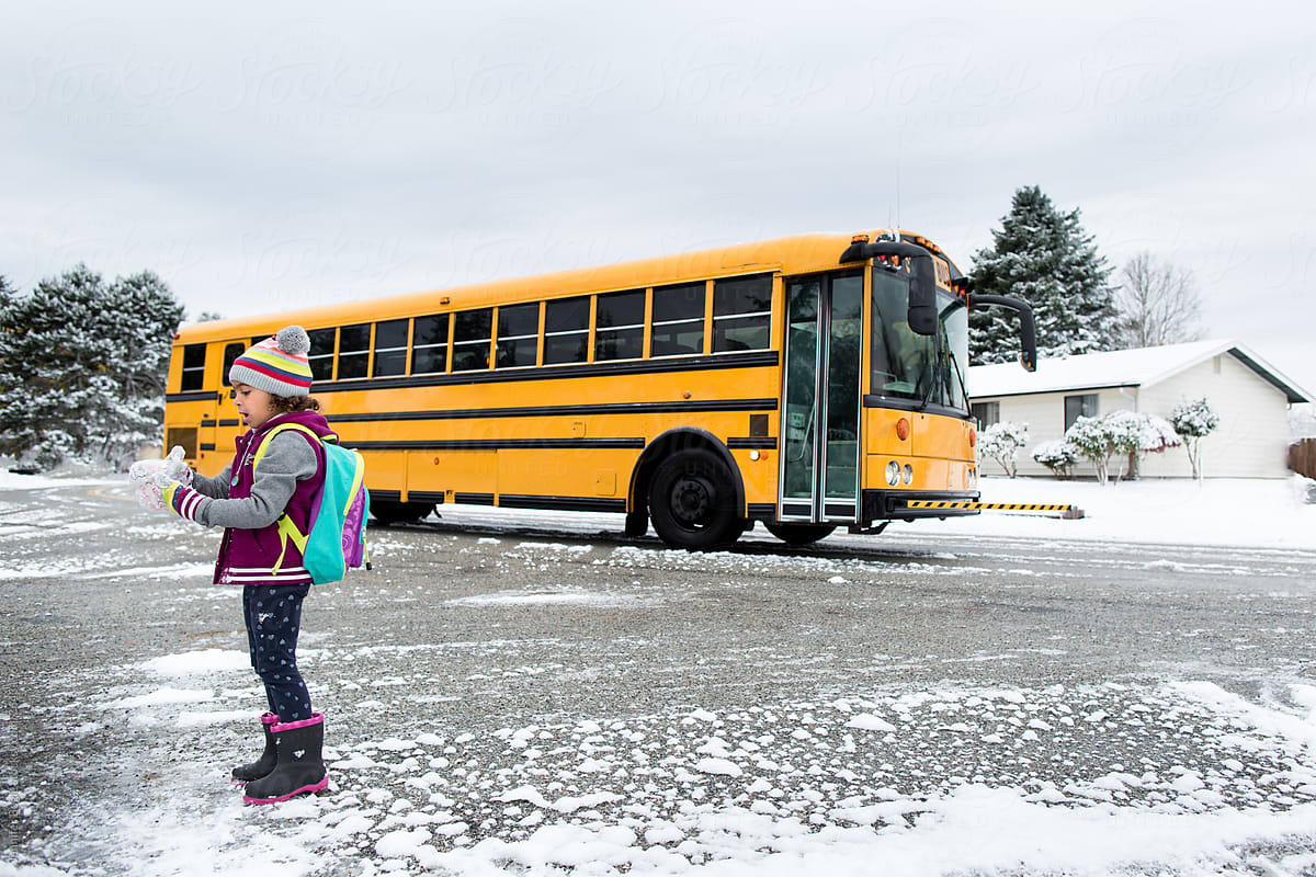 girl stands in front of school bus in snow