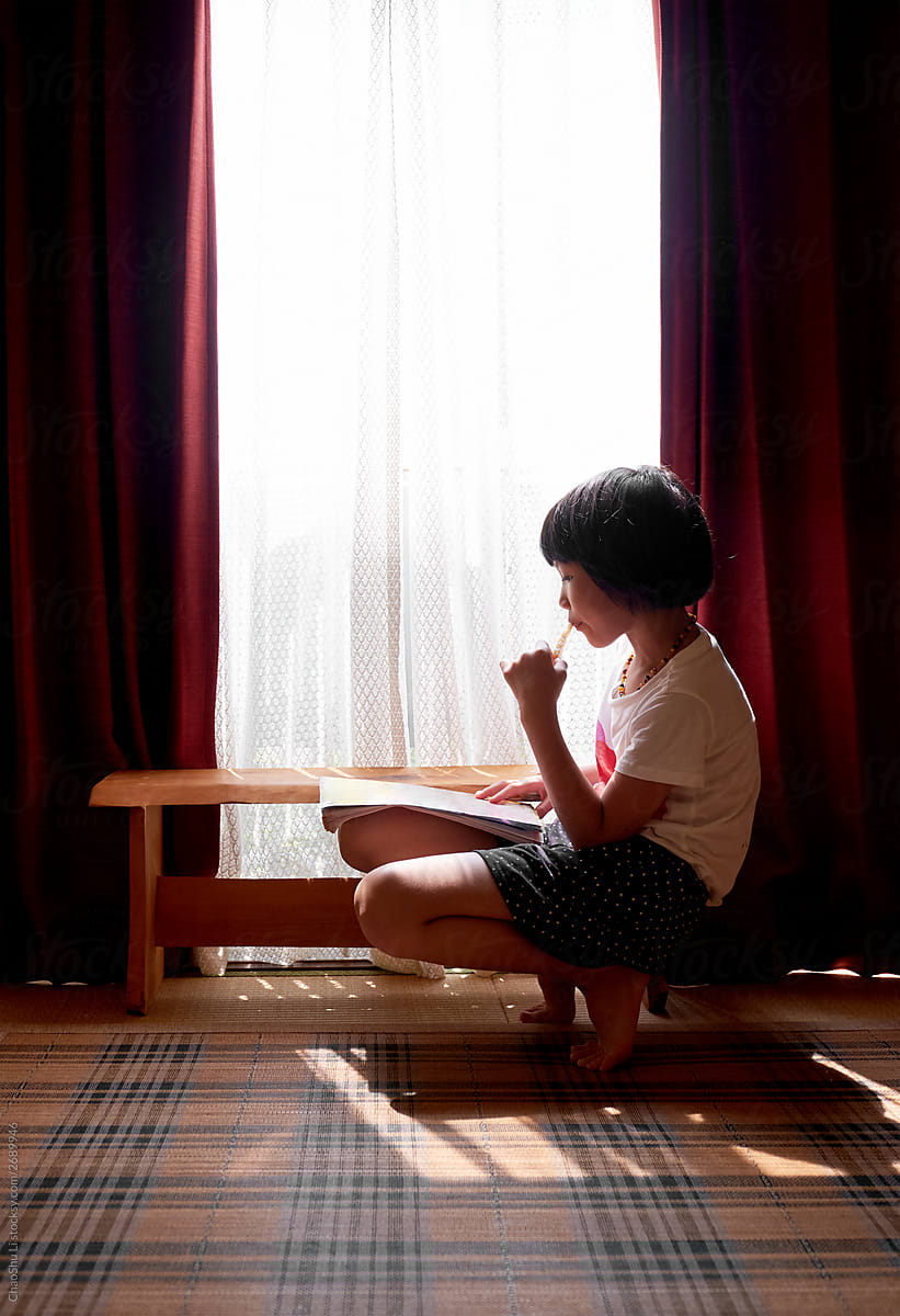Asian little girl reading by the window,