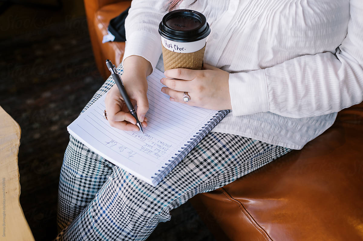 Woman holding beverage and writing down a to do list at a cafe
