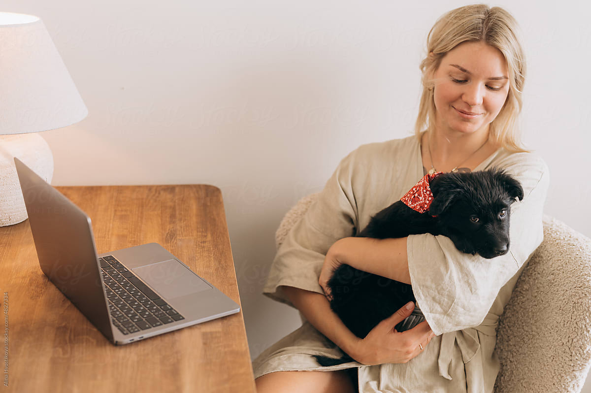 Smiling lady hugging dog at desk with netbook