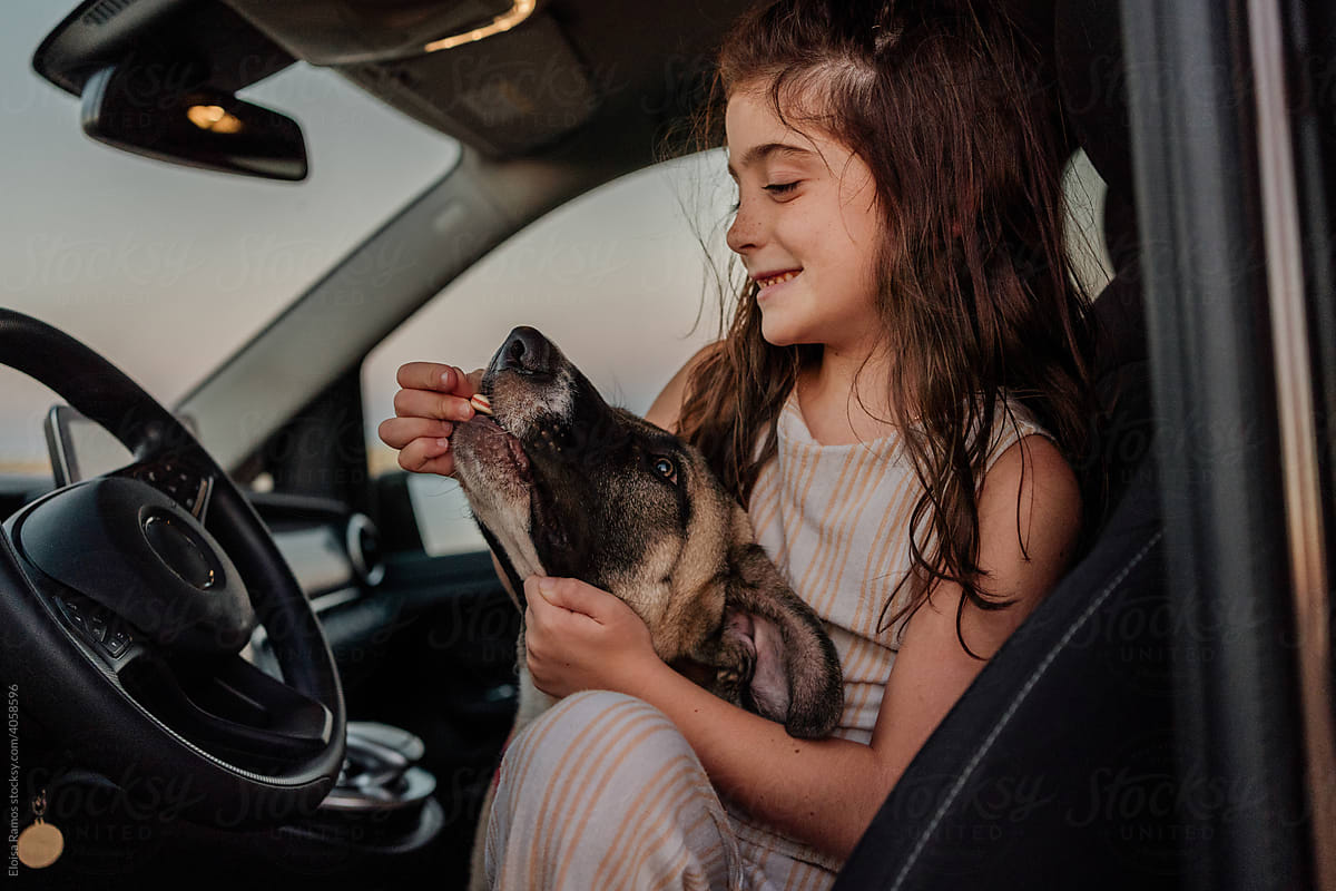 Girl feeding her dog inside a car