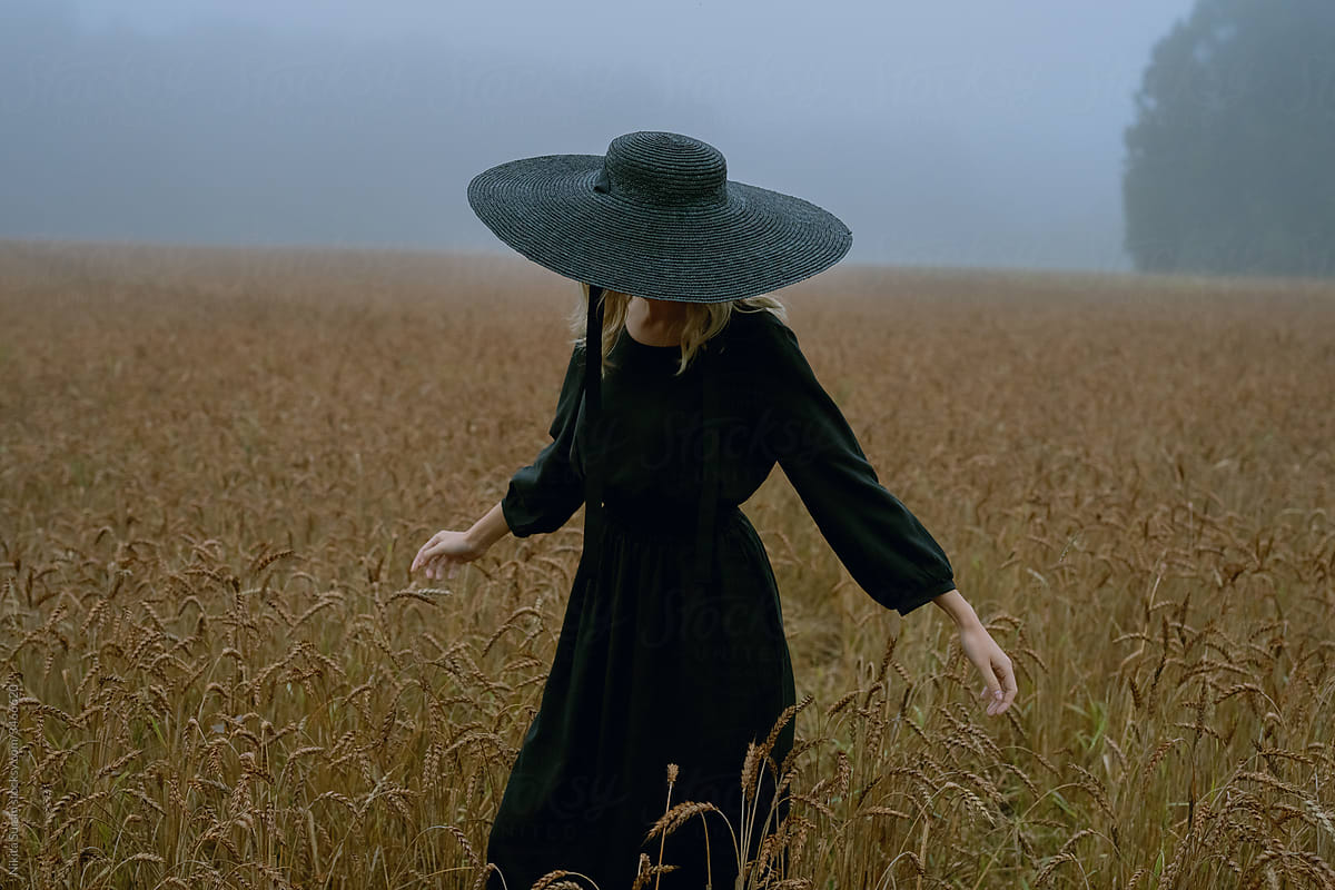 girl in a hat and black dress posing in a wheat field