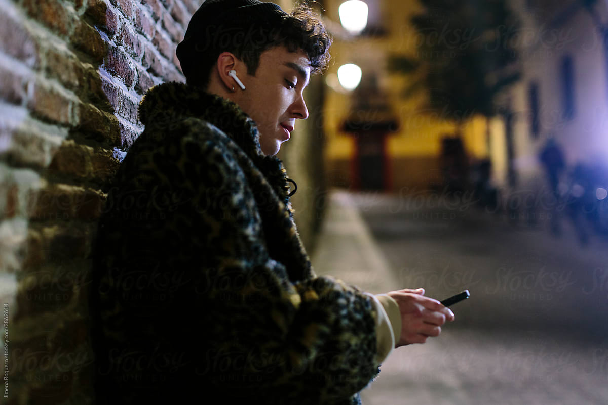 Young non-binary person at night  in the city listening to music on his smartphone