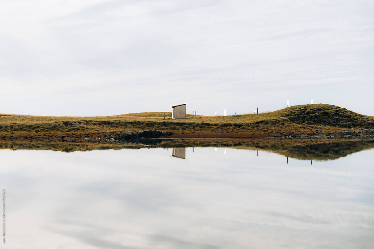 House around grassy land mirrored in water on horizon.Water Reflection