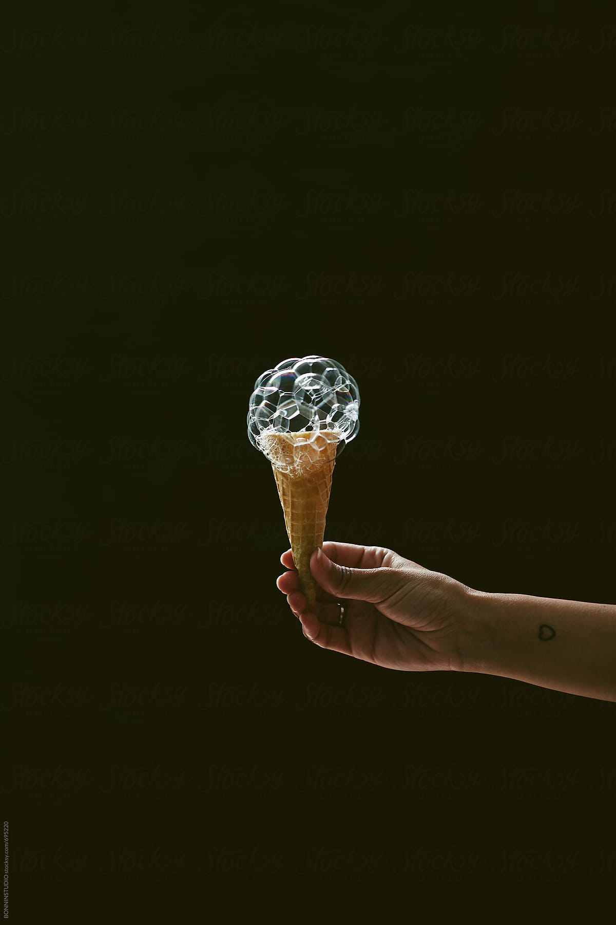Hand holding a soap bubble ice cream on a black background.
