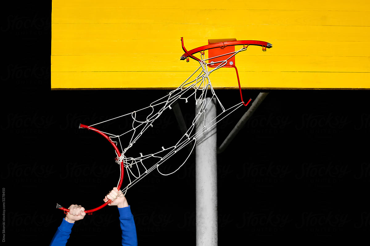 Hands holding a broken basketball hoop at night.