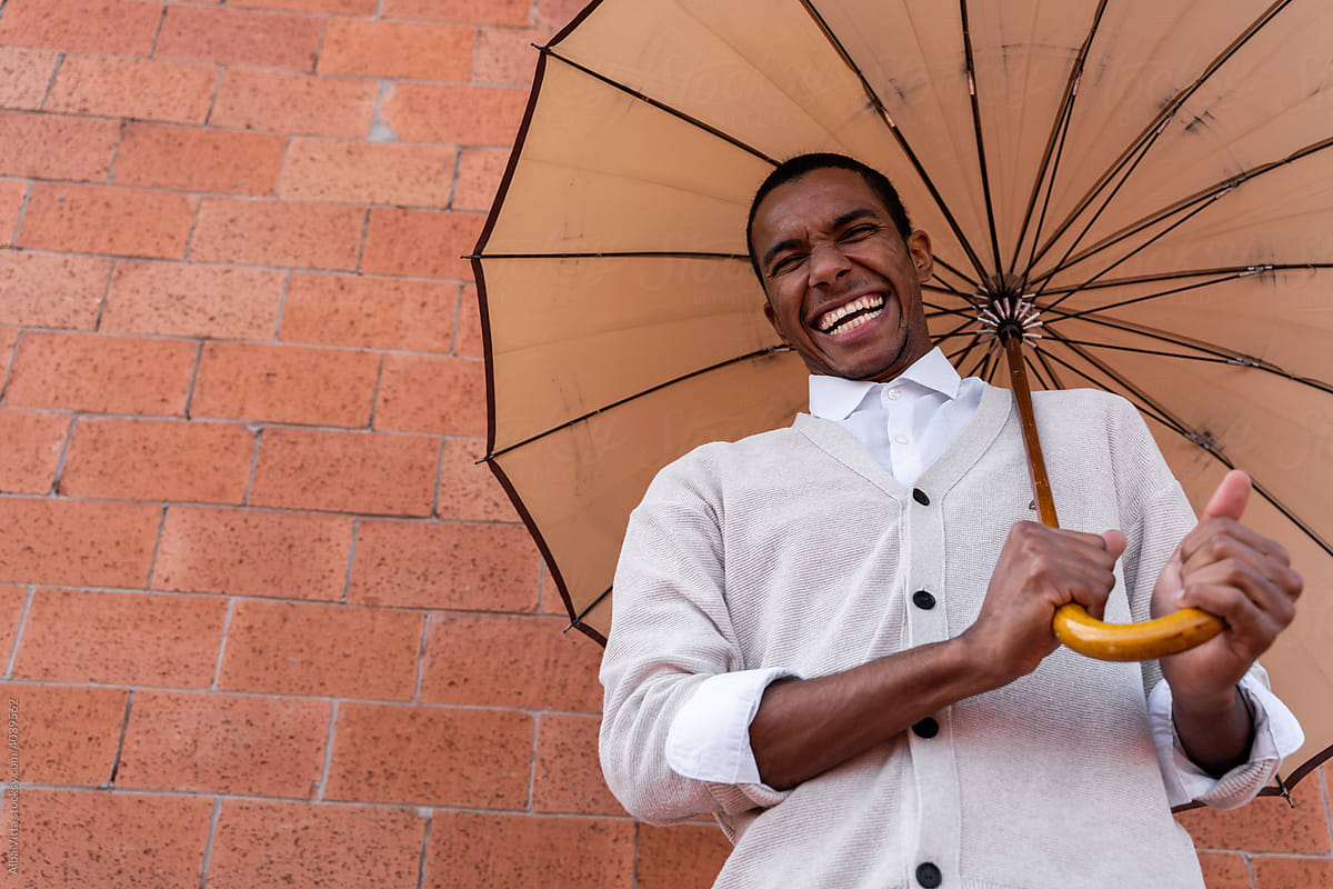 Black stylish man laughing posing with a parasol
