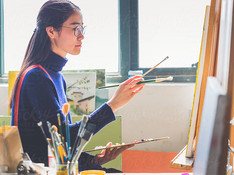 side view of a female artist painting in an art studio of college