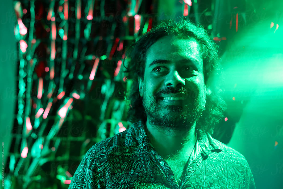 Long hair man smiling and looking up at alternative green neon party