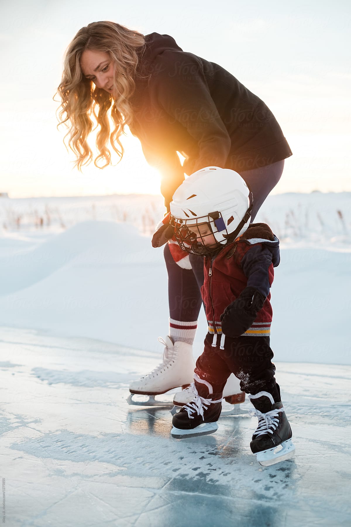A pretty Mother holds her son\'s hands while they skate on a frozen pond.