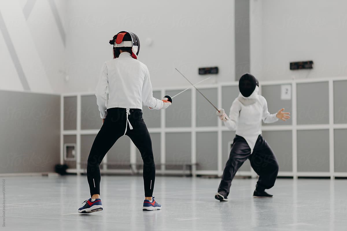 Anonymous sportswomen training with swords in fencing gym