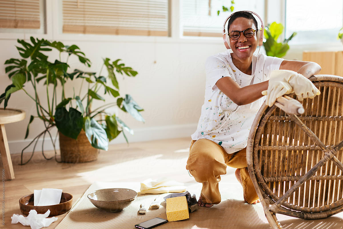 Cheerful black woman listening to music during furniture restoration