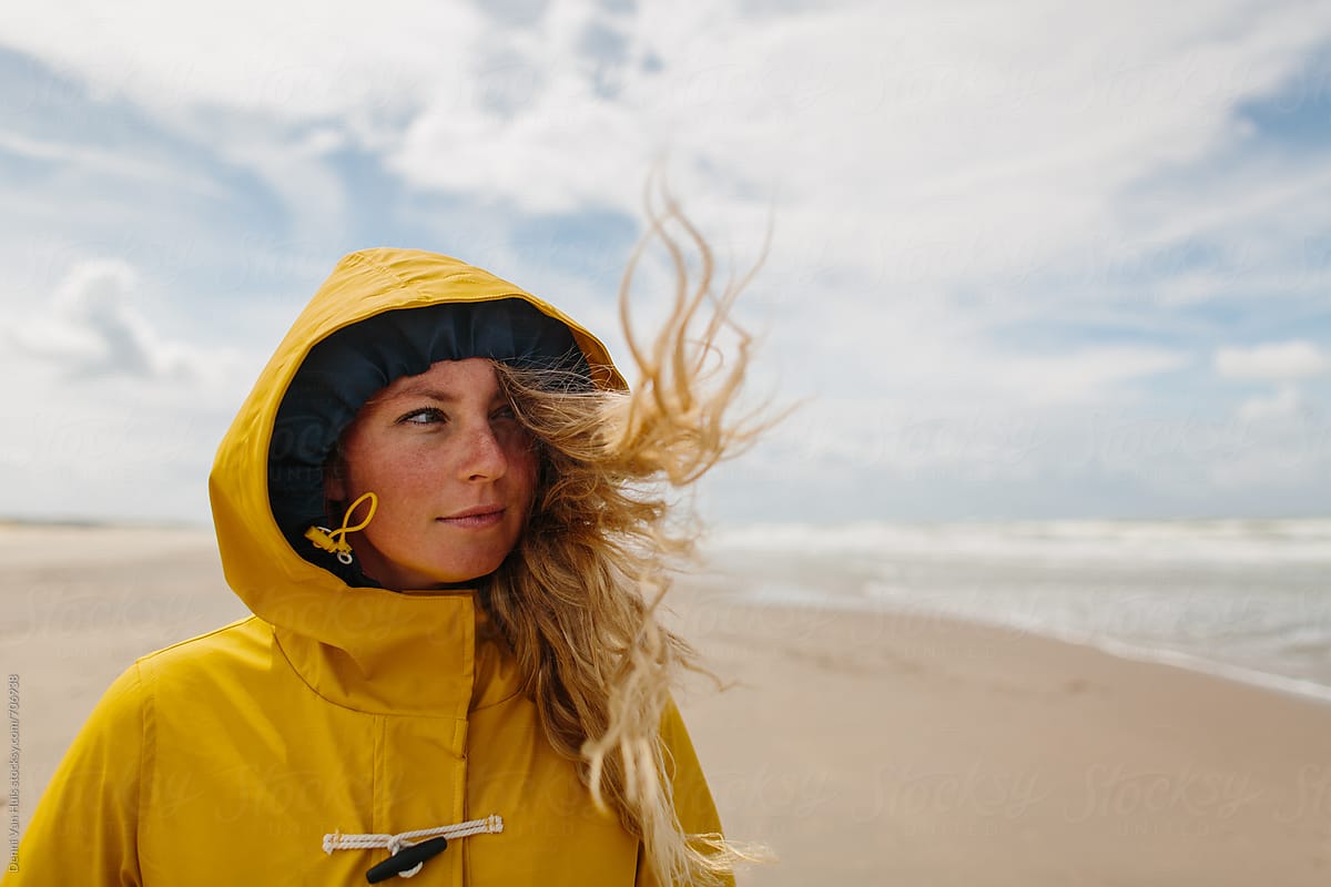 Woman on a windy beach wearing a yellow raincoat.