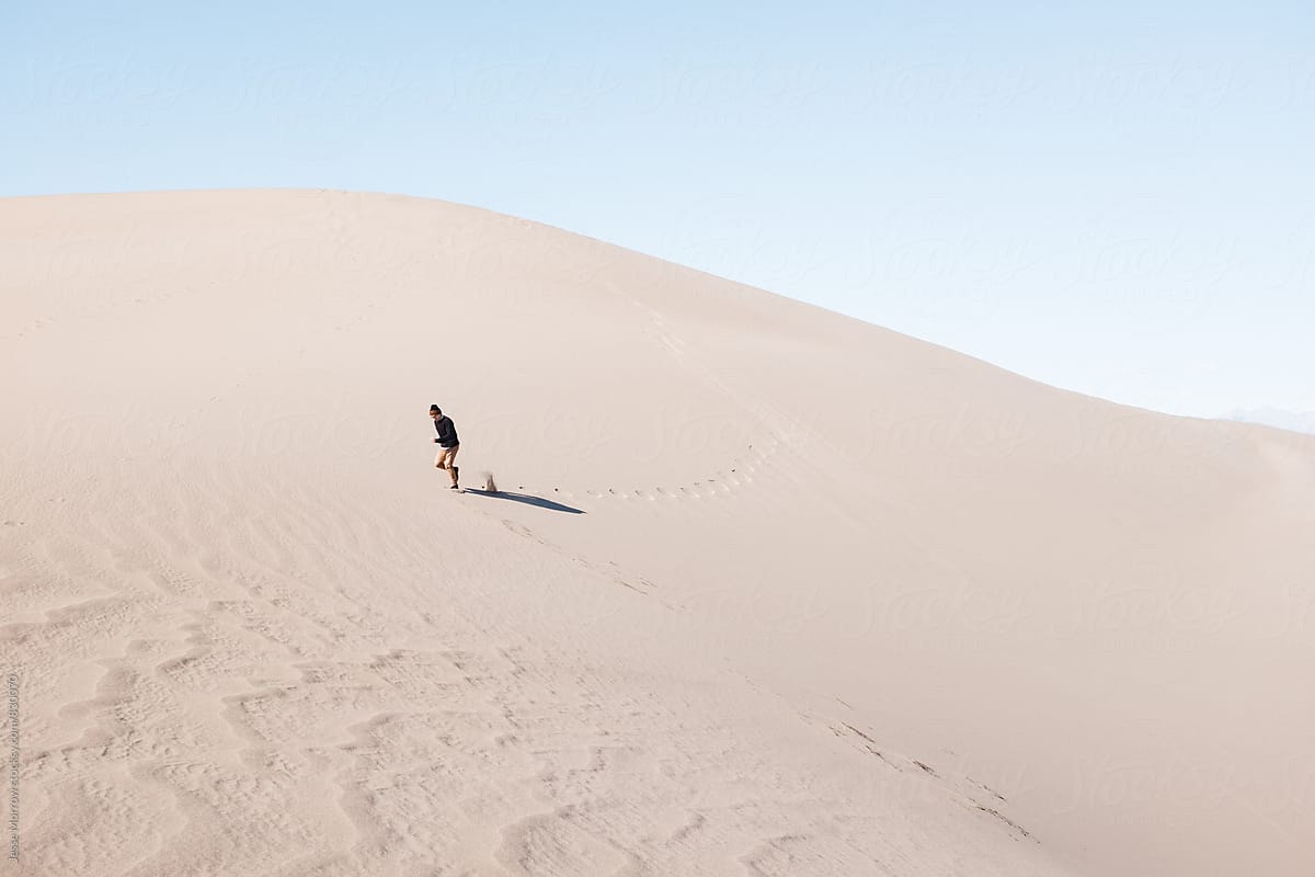 young man walking through sand dune desert alone