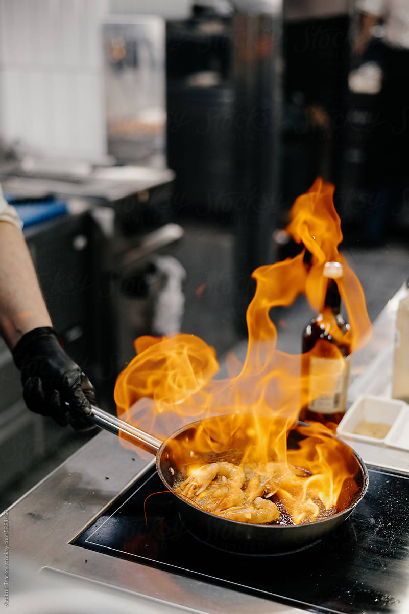 Anonymous chef preparing prawns in burning frying pan