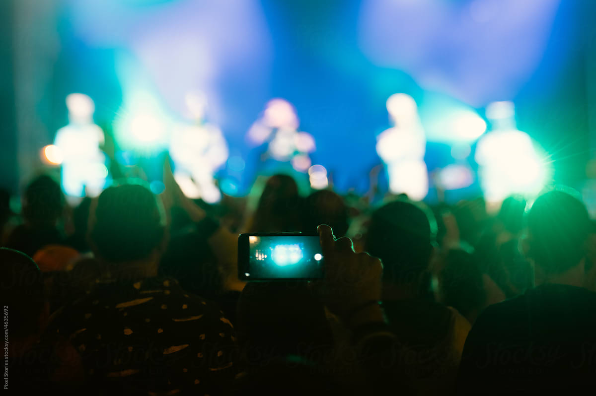Anonymous crowd at a concert. Person taking photos using smartphone.