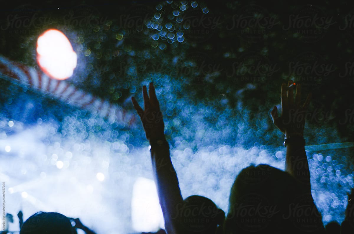 Girl in the crowd rising hands in a music show with a cigarette in her hand