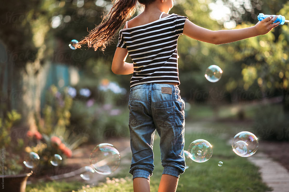 Young girl is playing with bubbles in a yard.