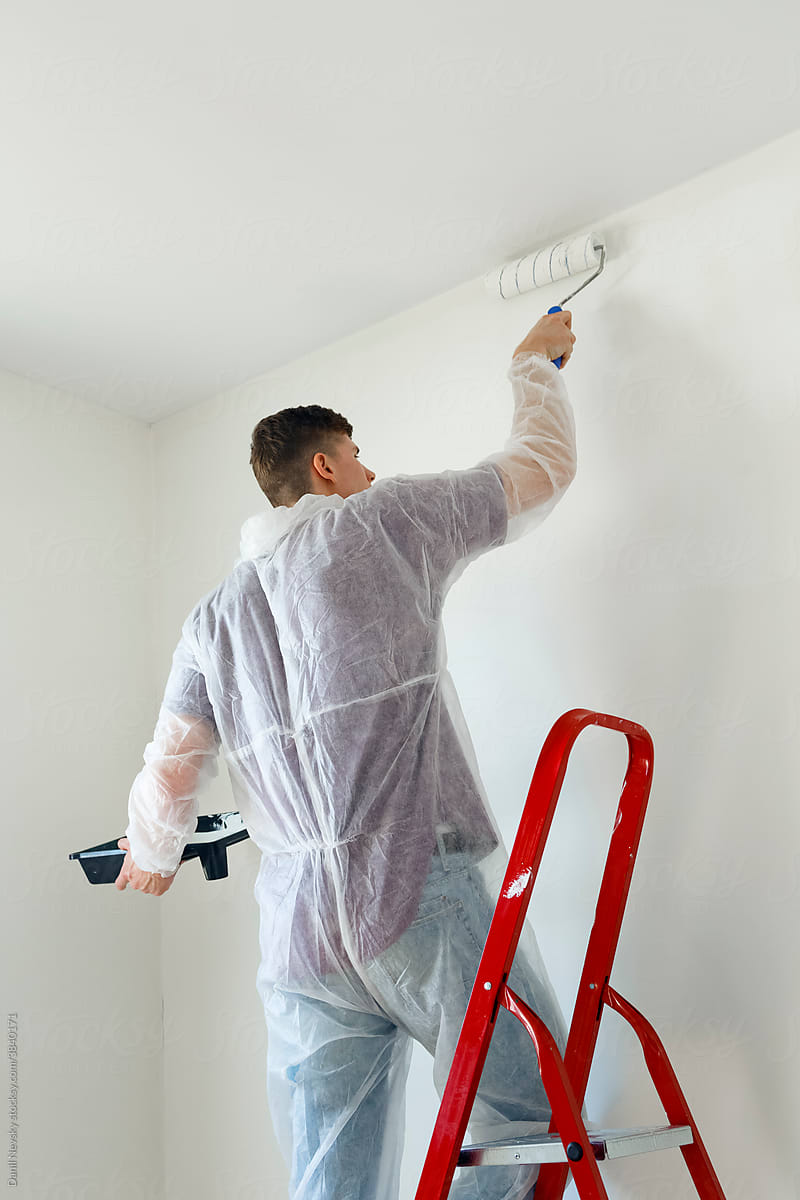 Man with roller painting wall in room