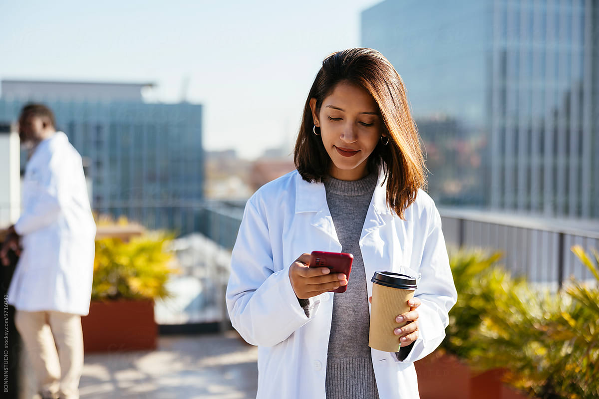 Doctor with coffee to go using smartphone