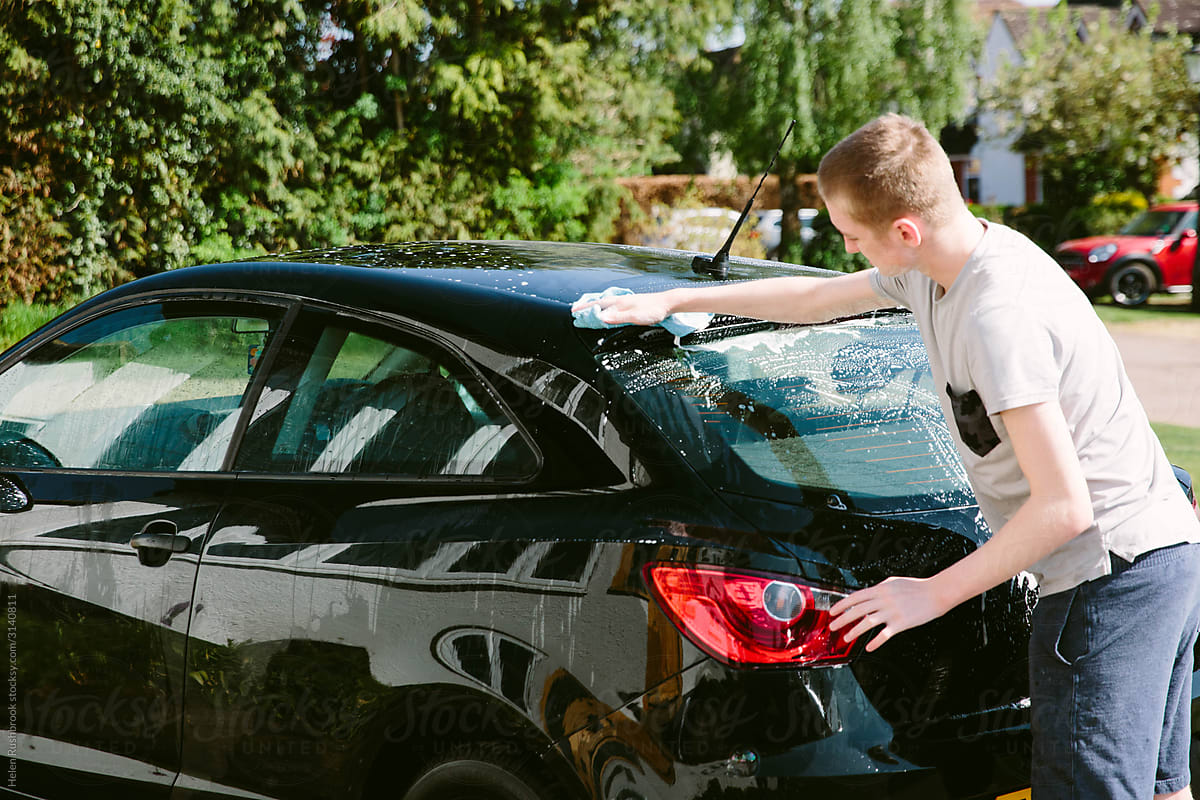 Teenage boy washing his first car on a suburban street
