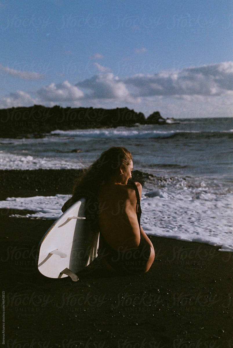 woman on black sand beach with her surfboard