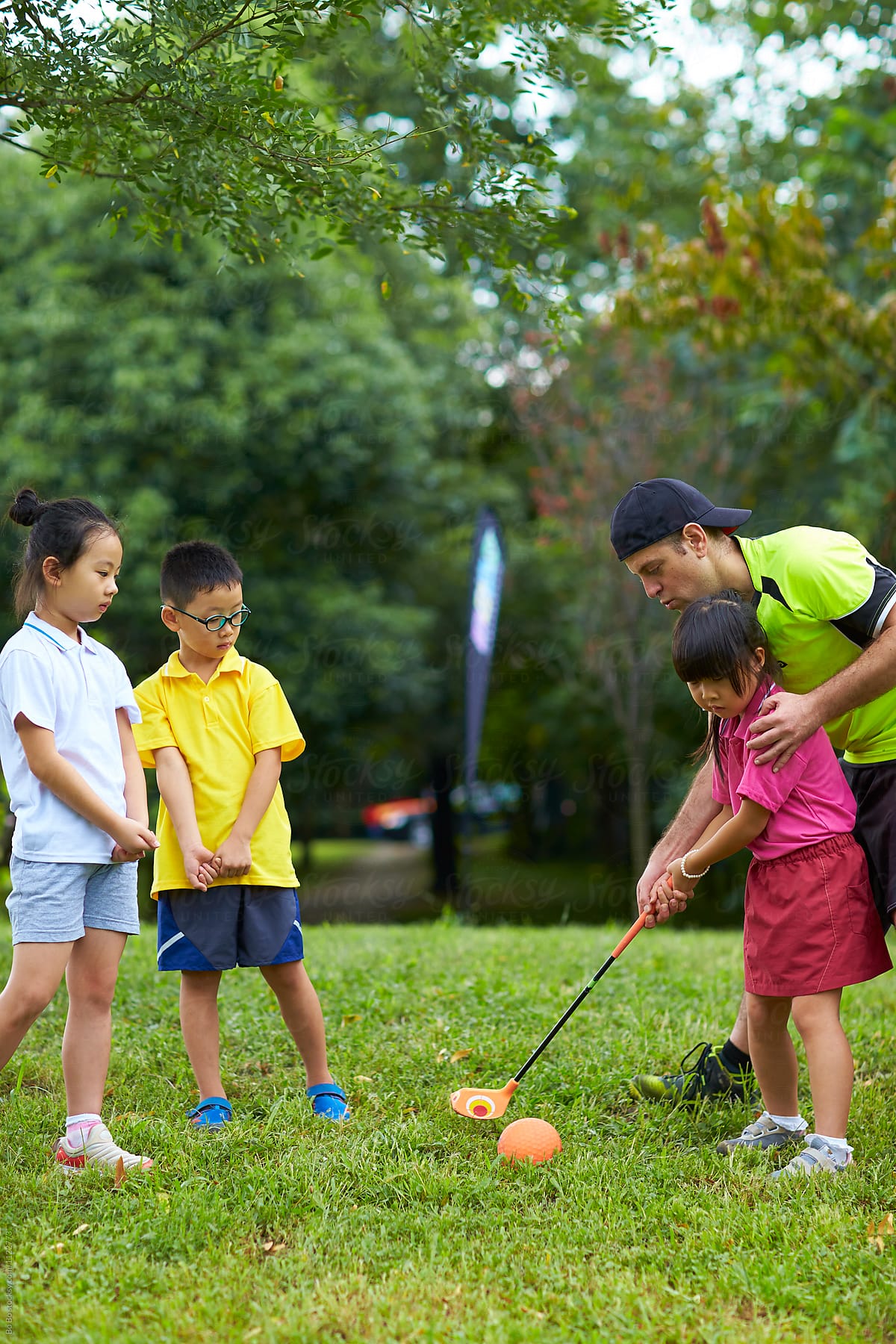 Caucasian English teacher teaching  Chinese kids  golf outdoor in the park