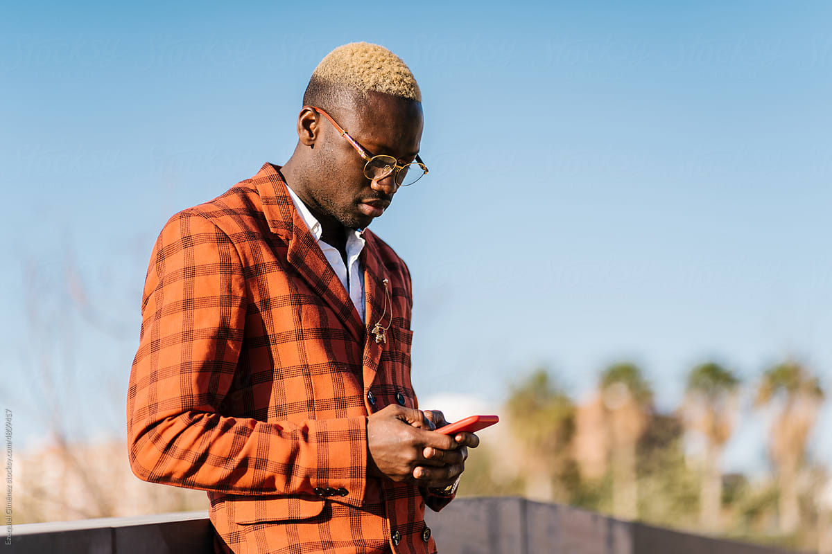 Focused stylish black man using smartphone on street